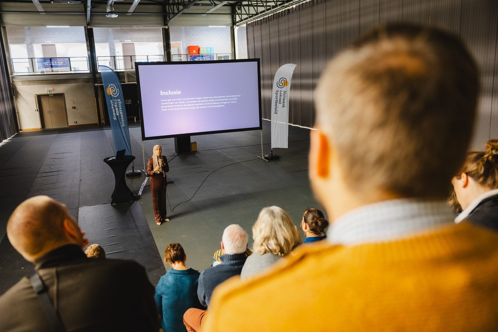 Sana Sellami tijdens een keynote voor Netwerk Lokaal Sportbeleid, met publiek op tribune